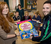 Two students holding an Irish language book in front of a class and lecturer