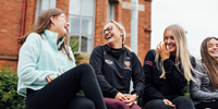 Picture of four students sitting outside of St Mary's university college laughing