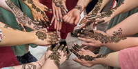 A circle of hands all coming together in the middle.  Each hand is intricately tattooed with a henna design.